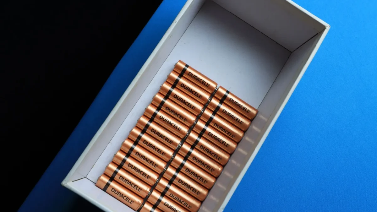 Top view of neatly arranged batteries in a box on a contrasting blue surface.