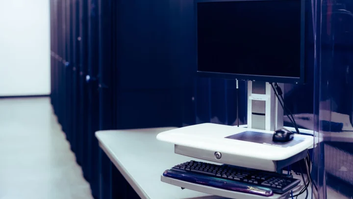Contemporary computer with black screen placed on stand near row of server steel racks in data center