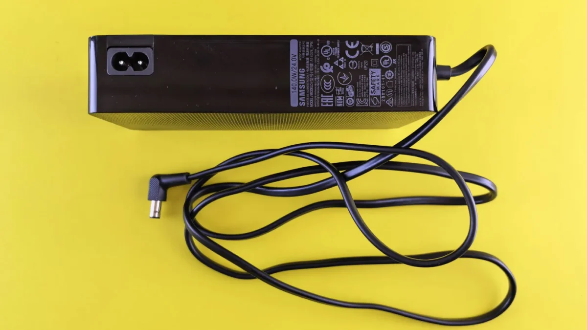 Flat lay of a black power adapter and cord on a vibrant yellow background.