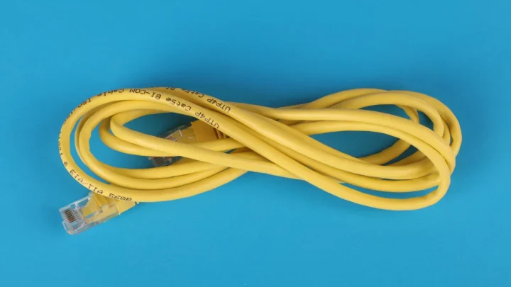 High-angle view of a yellow ethernet cable on a bright blue background.