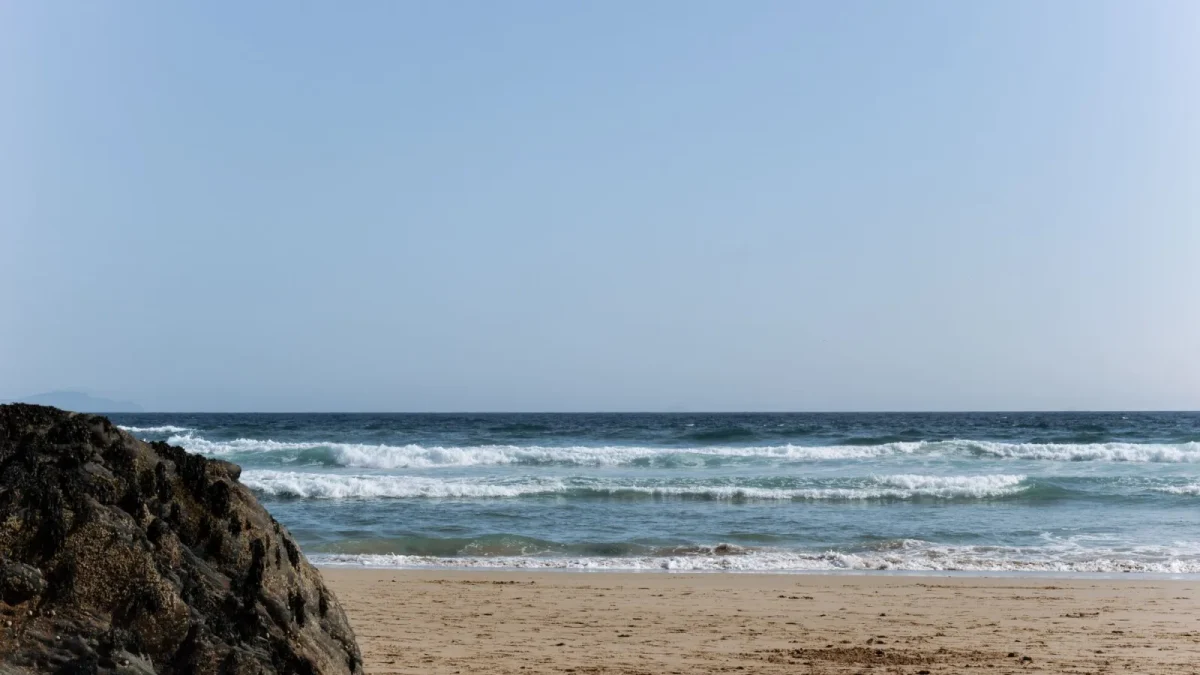 Peaceful sandy beach scene with ocean waves and a large rock, perfect for relaxation concepts.