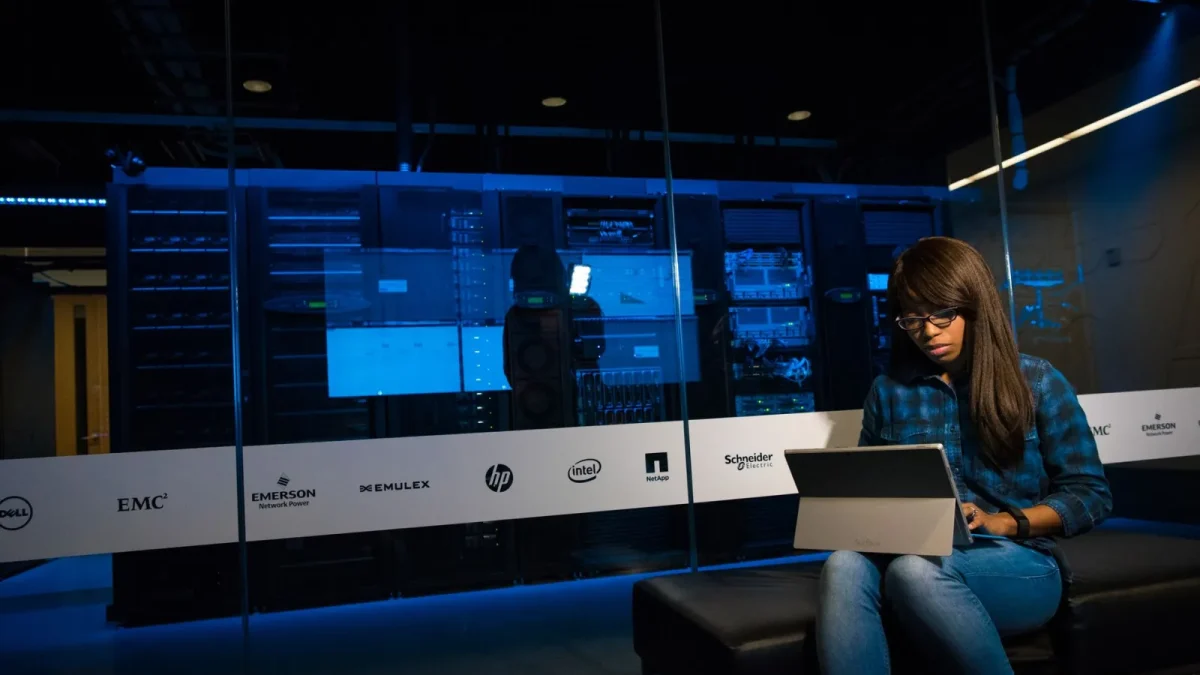 Woman using a laptop in a server room, showcasing modern technology and work environment.