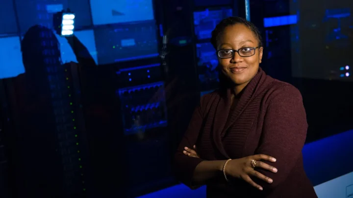 Professional woman standing confidently in a data center, surrounded by glowing servers.
