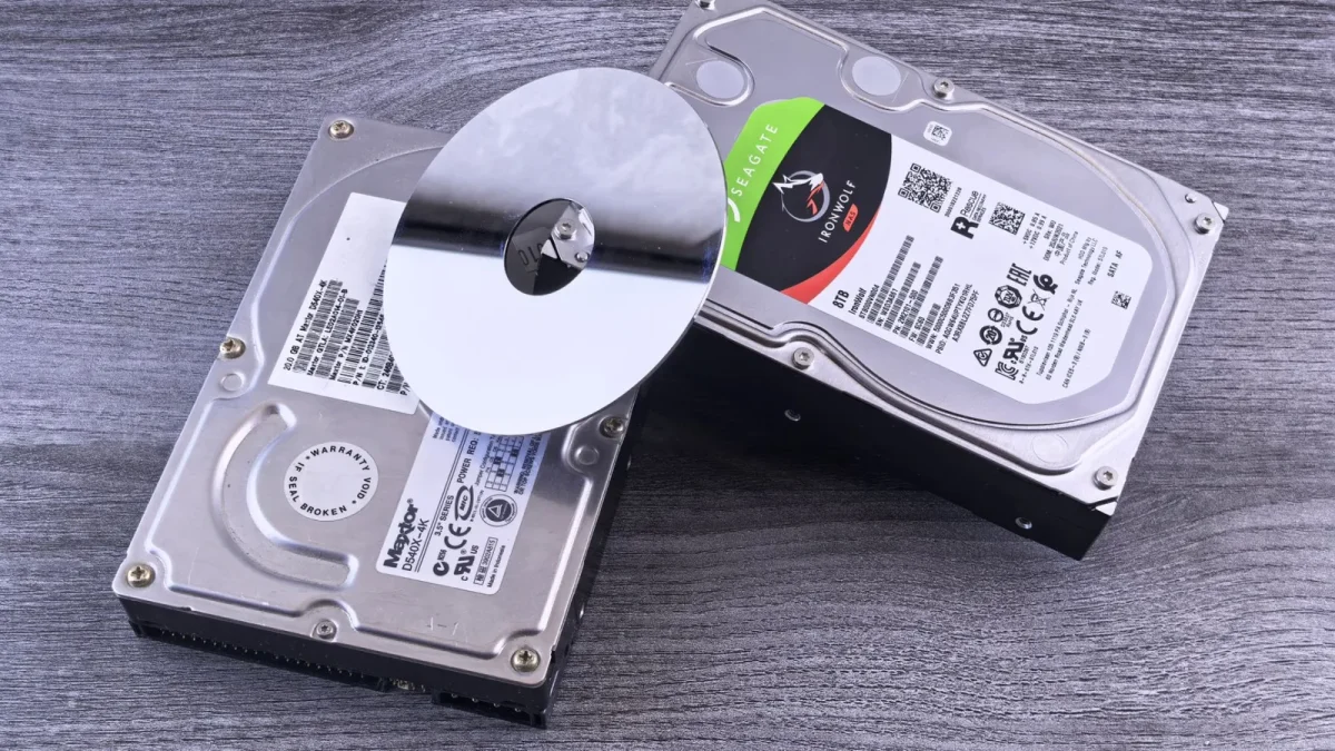 Two computer hard drives and a shiny disk displayed on a wooden surface.