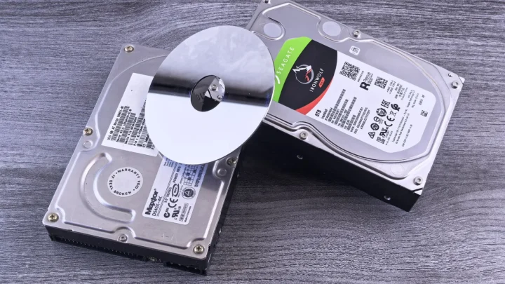 Two computer hard drives and a shiny disk displayed on a wooden surface.
