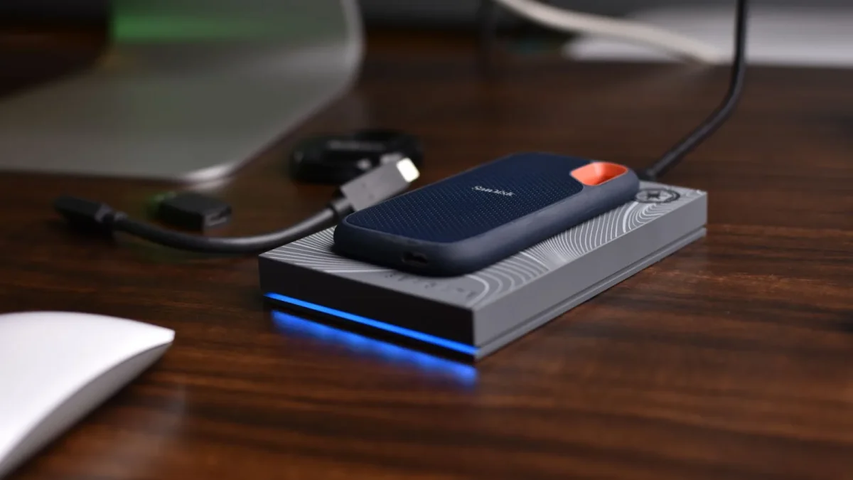 A close-up view of a portable USB SSD placed on a wooden desk with connected cables.