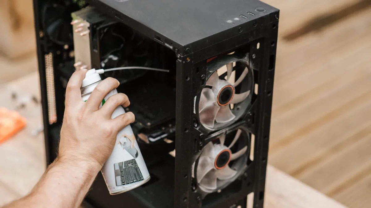 Crop anonymous male with compressed air can removing dust from computer system unit