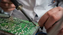 Technician performing precise soldering on a circuit board for electronics repair.