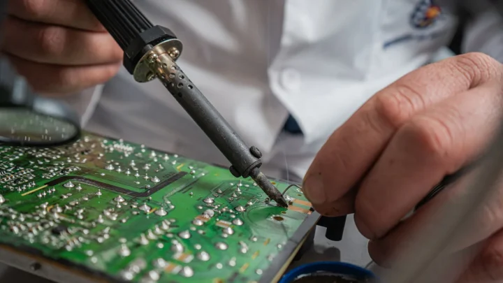 Technician performing precise soldering on a circuit board for electronics repair.