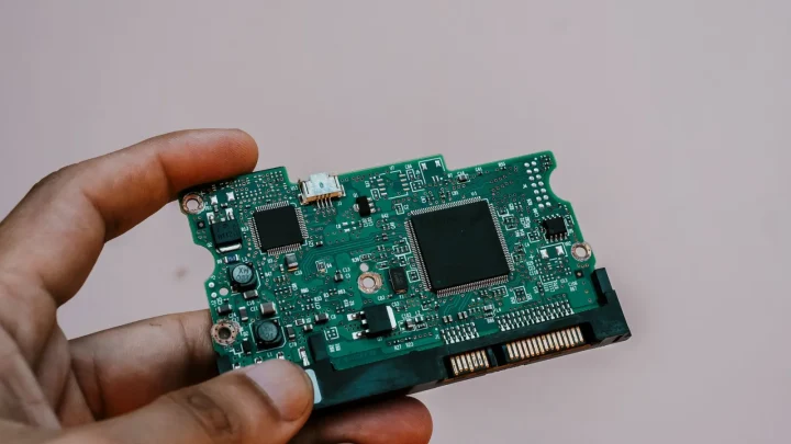 Close-up image of a hand holding a circuit board from a hard drive, showcasing electronic technology.