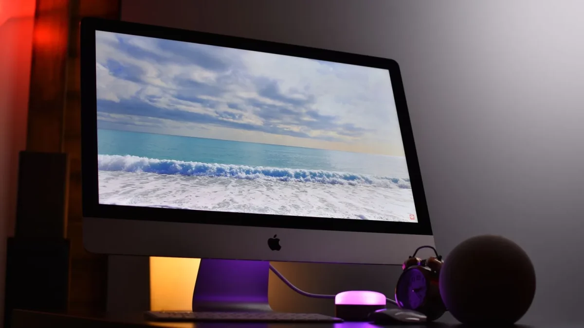 Apple iMac displaying ocean view. Elegant workspace with ambient lighting.
