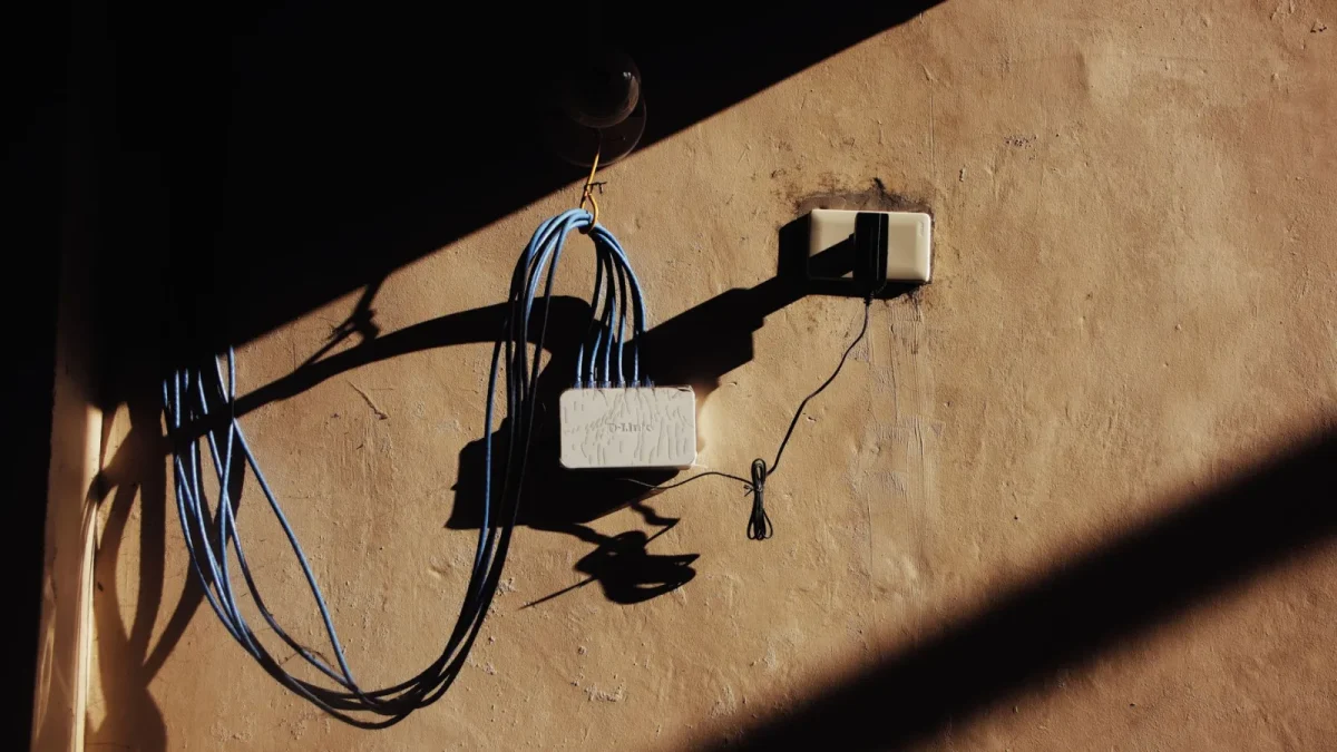Electric blue wires connected to network adapter plugged in socket on shabby brown wall of building on street with shado