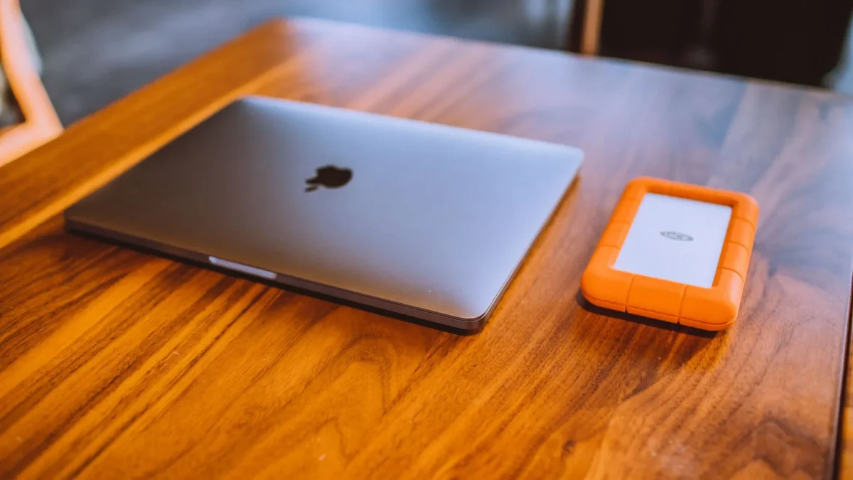 A sleek laptop and rugged external hard drive on a stylish wooden table indoors.