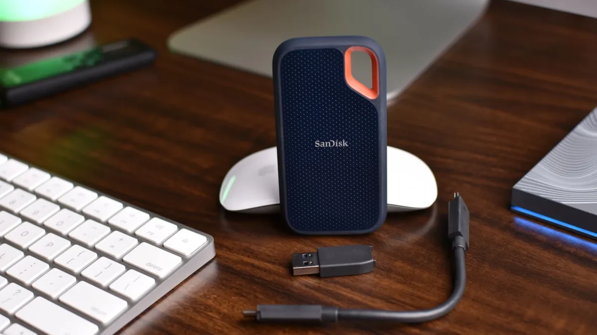SanDisk portable SSD with USB cable and computer accessories on a wooden desk.